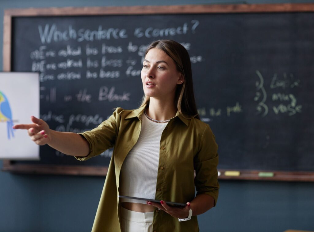 Female Teacher with Table Speaking to Student in English Class at Language School