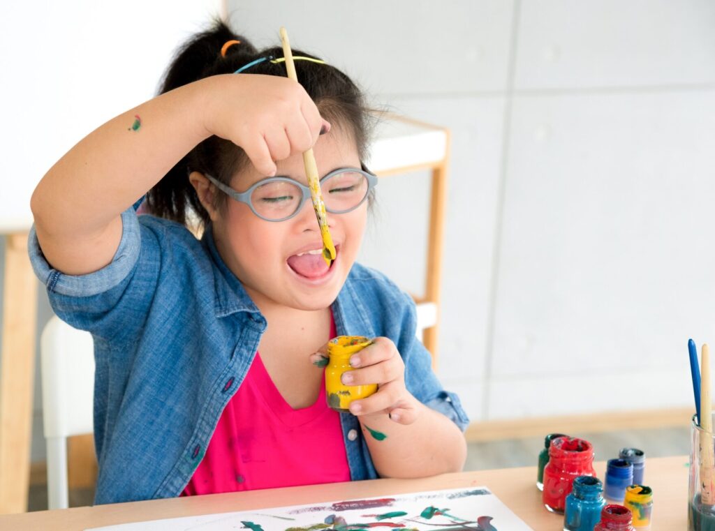 Young autism disabled child complex genetic disorders kid drawing a picture by watercolor.